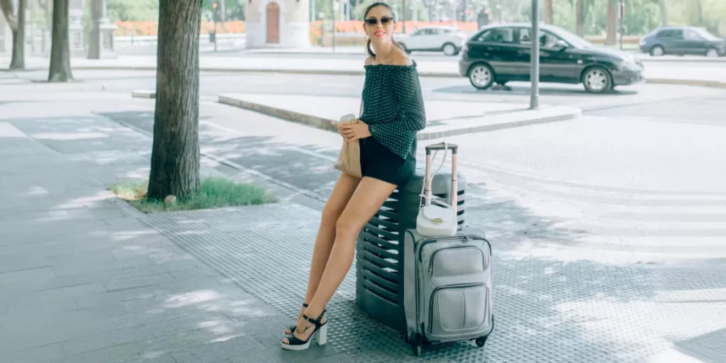 Frau mit Sonnenbrille sitzt auf ihrem kleinen Handgepäck