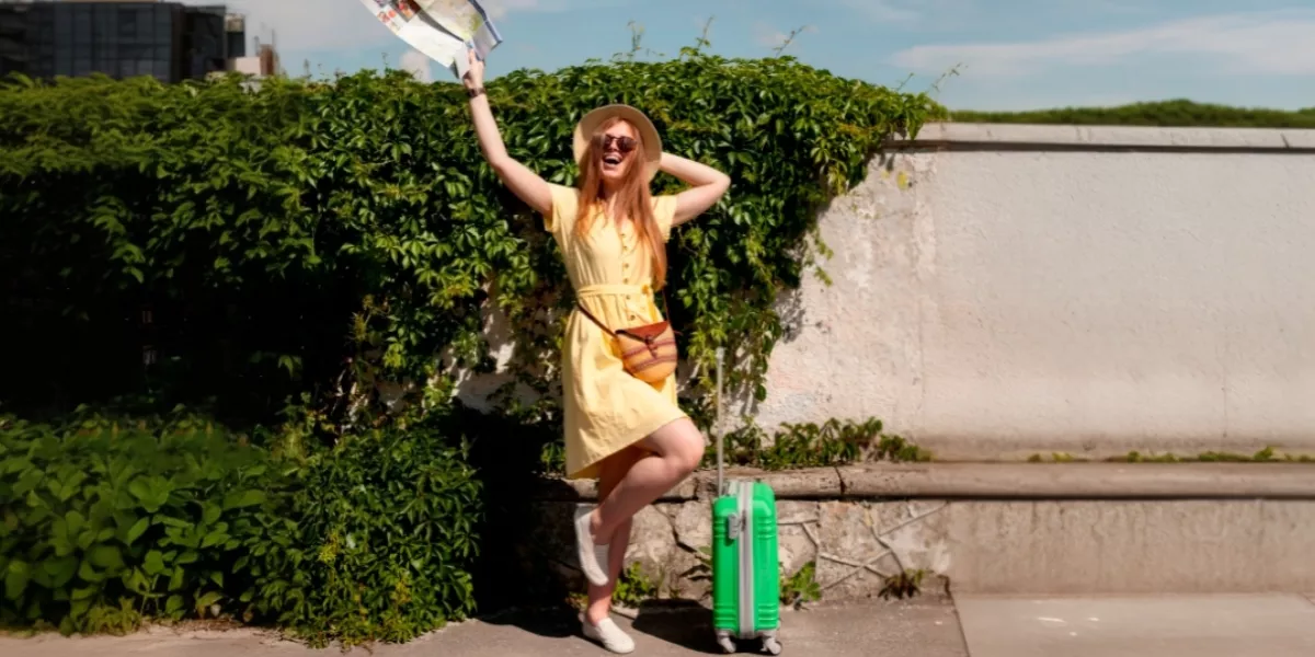 Frau im gelben Kleid mit grünem Koffer an einem sonnigen Tag
