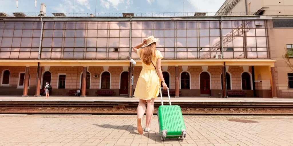 Frau in gelbem Kleid und grünem Koffer an einem Bahnhof